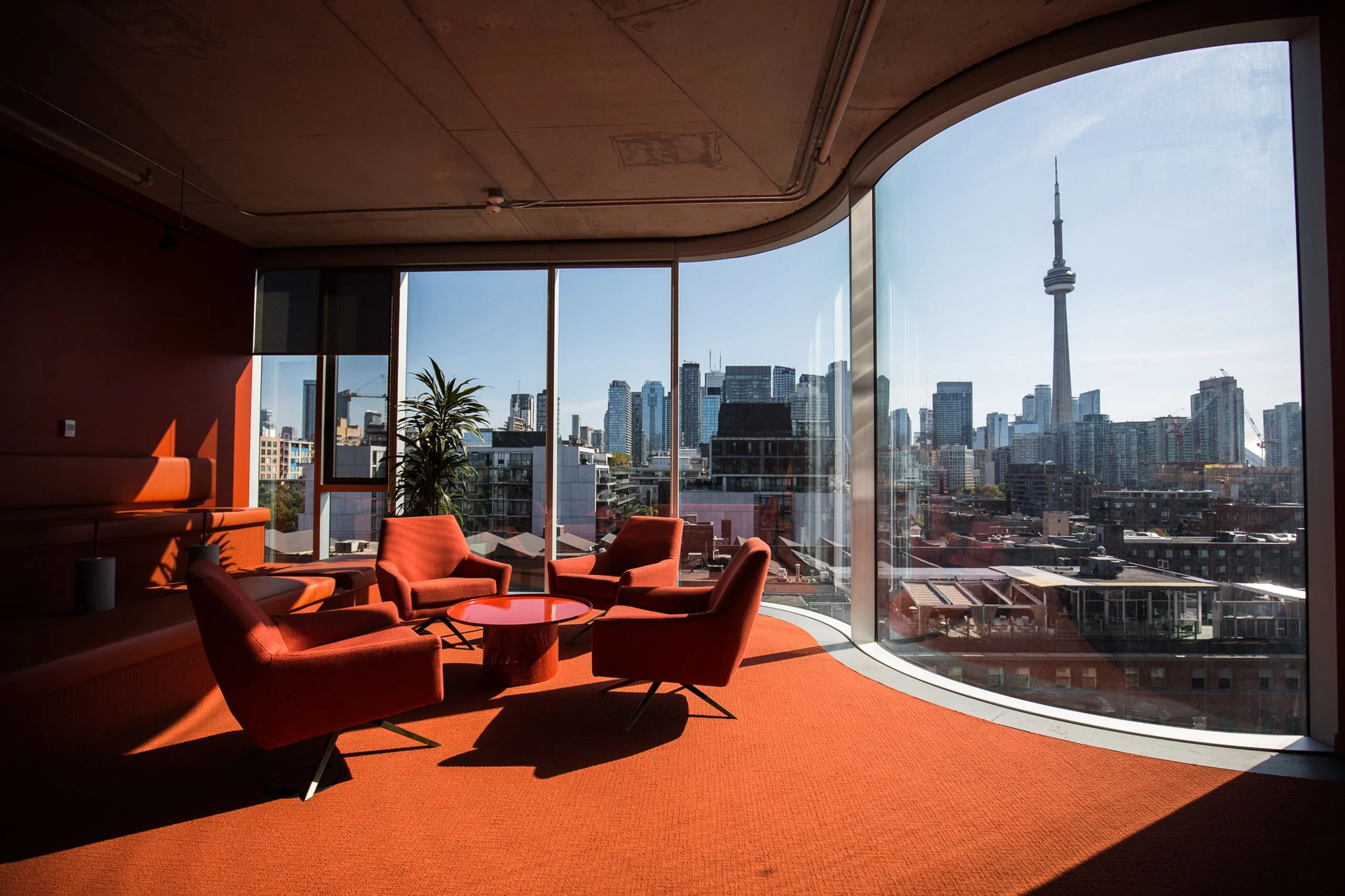 Burnt-orange lounge nook with curved floor-to-ceiling glazing overlooking the CN Tower and the Toronto skyline