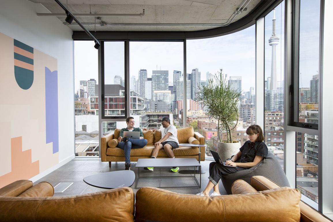 Tan-leather lounge with a colour-block mural and people working against the Toronto skyline