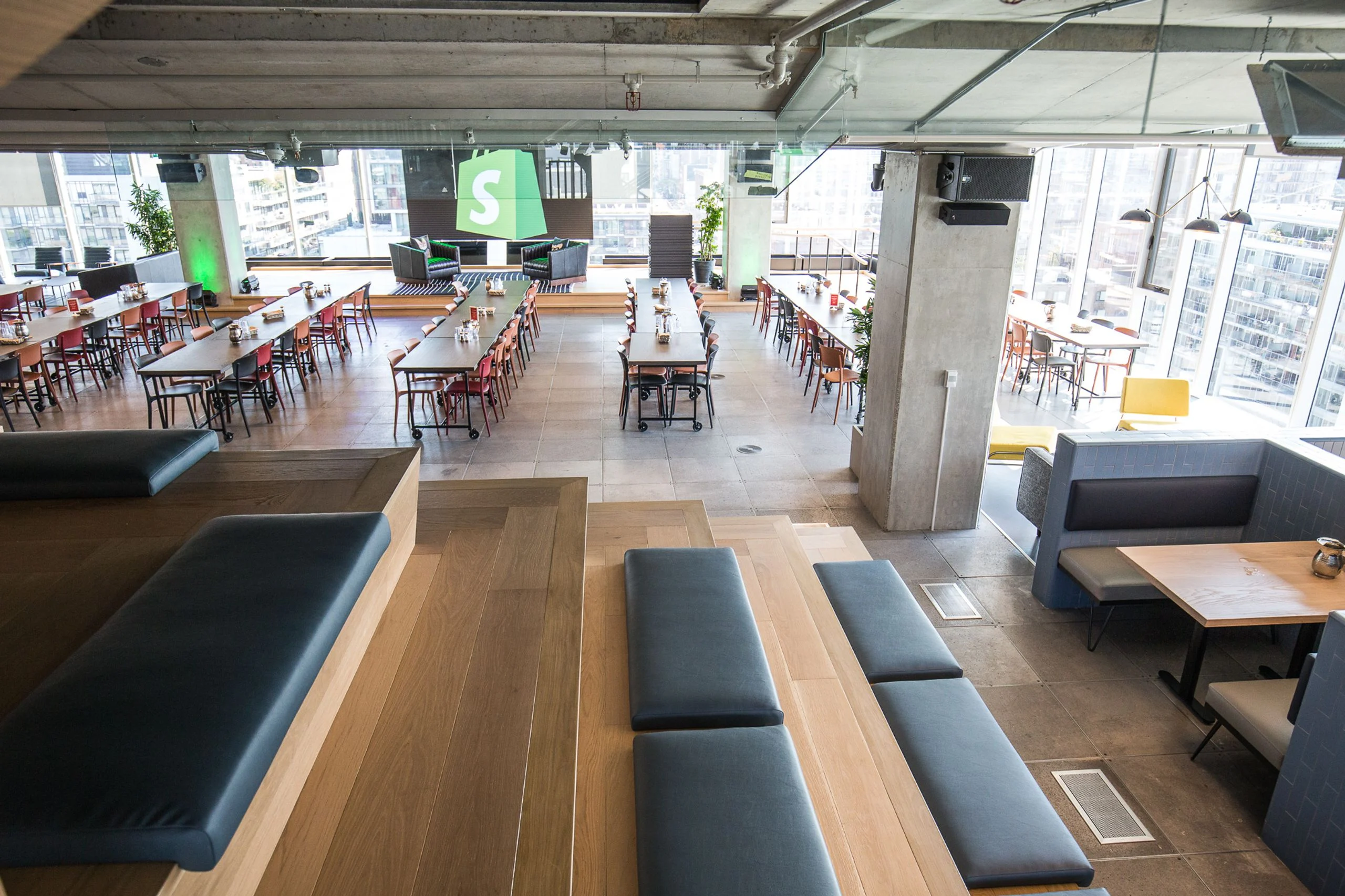 A tiered all-hands social space with a large green Shopify logo and banquette seating