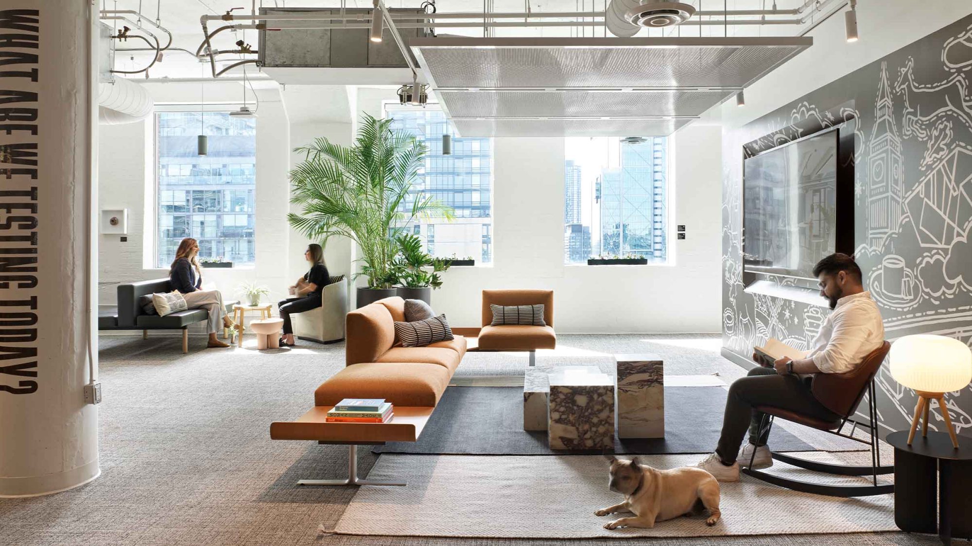 M Moser workplace — a bright, plant-filled lab office with tan sofas, a London-themed mural wall, people working, and a dog